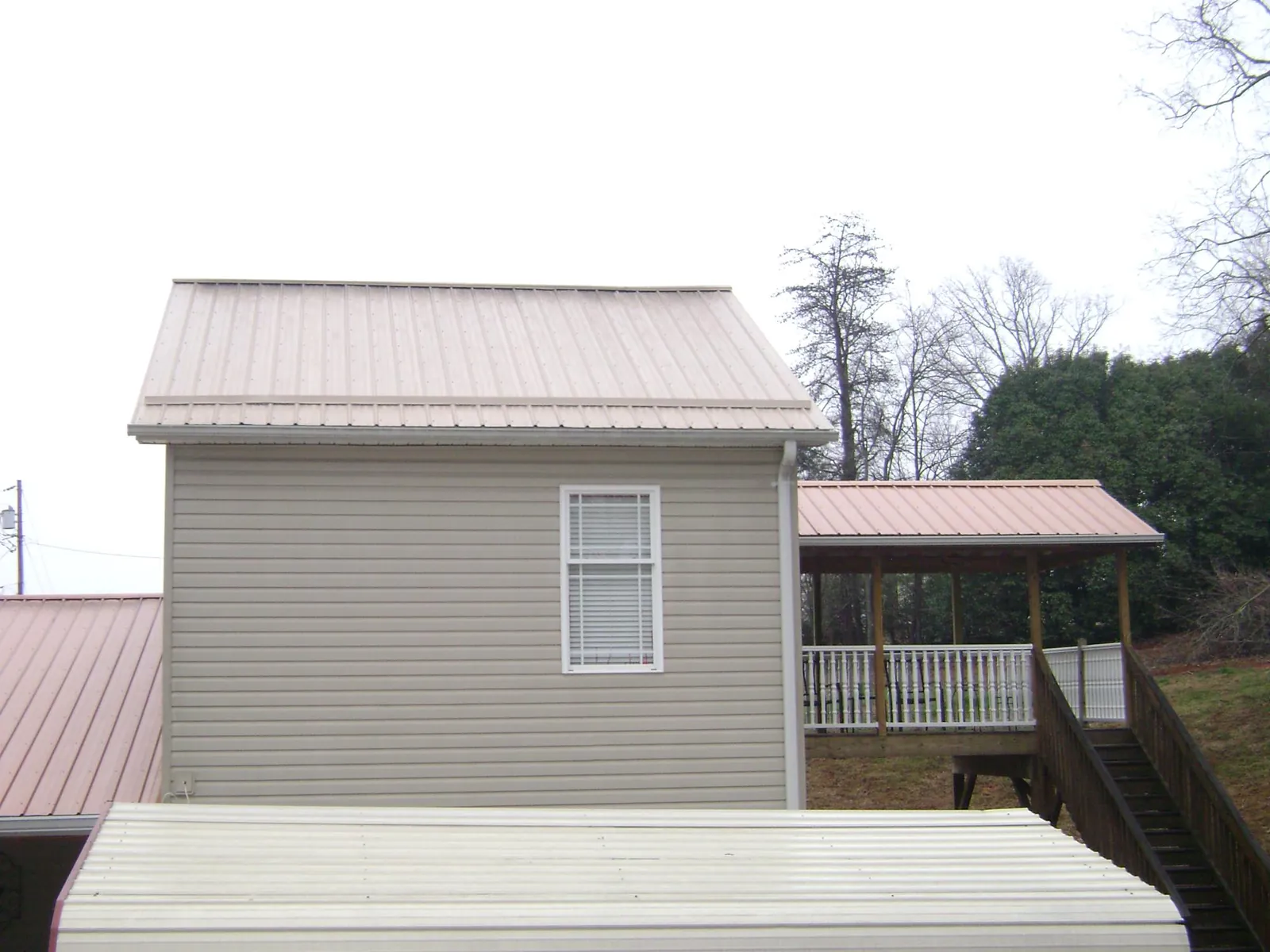 Tan metal roofs on a two story addition and attached porch, from a Roof Replacement job in Humboldt
